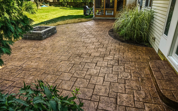 Brown stamped concrete patio with a rectangular stone pattern beside a landscaped garden