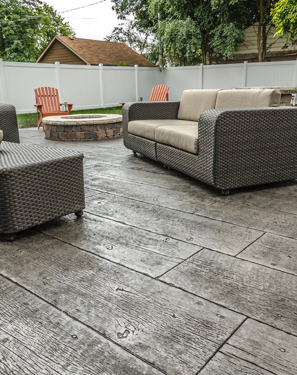 Gray wood-plank stamped concrete patio with visible grain, outdoor seating, and a circular fire pit